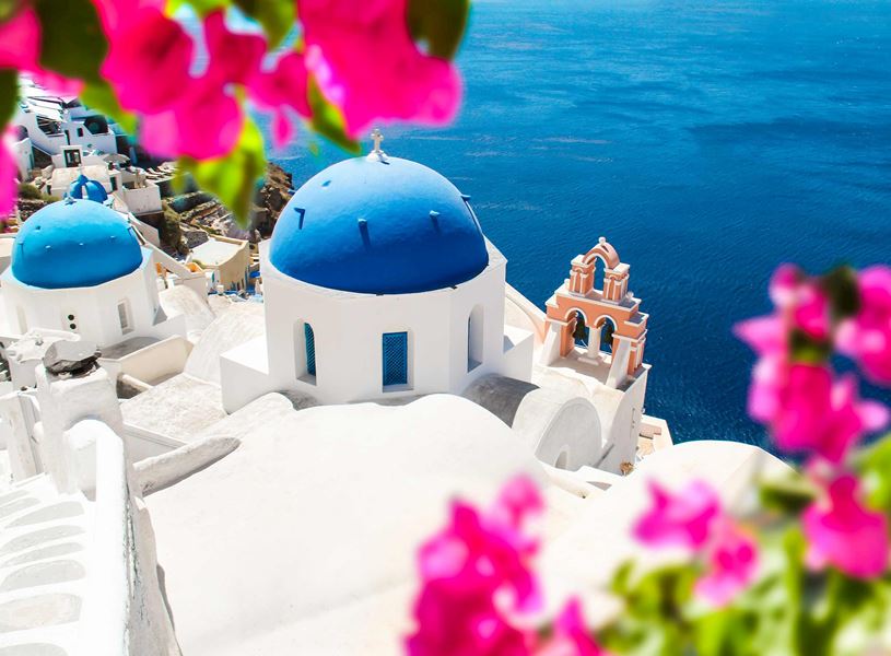 Blue domed church framed by vibrant pink bougainvillaea flowers, Santorini, Greece