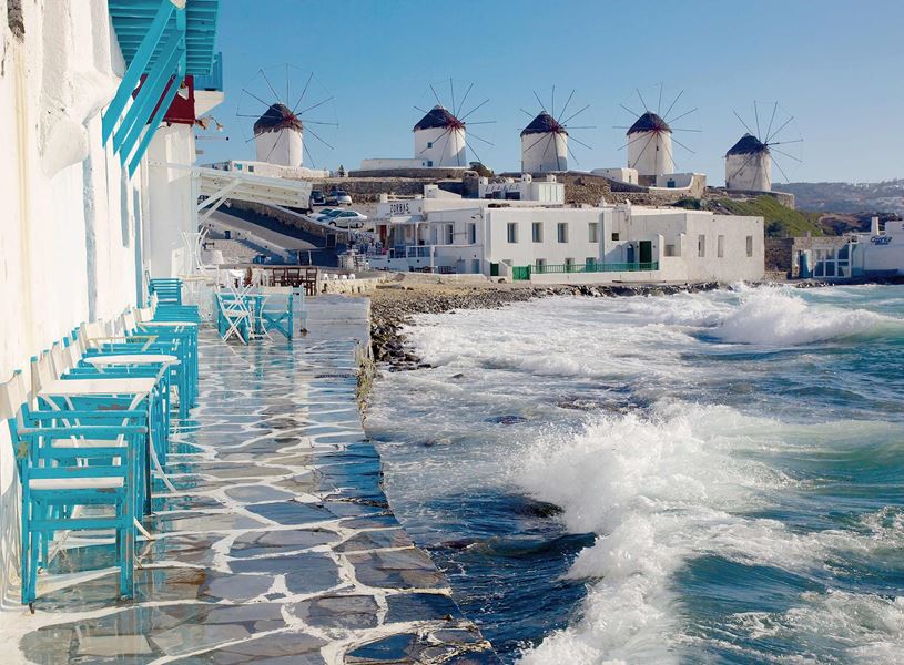 White windmills overlooking blue sea with waves crashing on shore, Mykonos, Greece