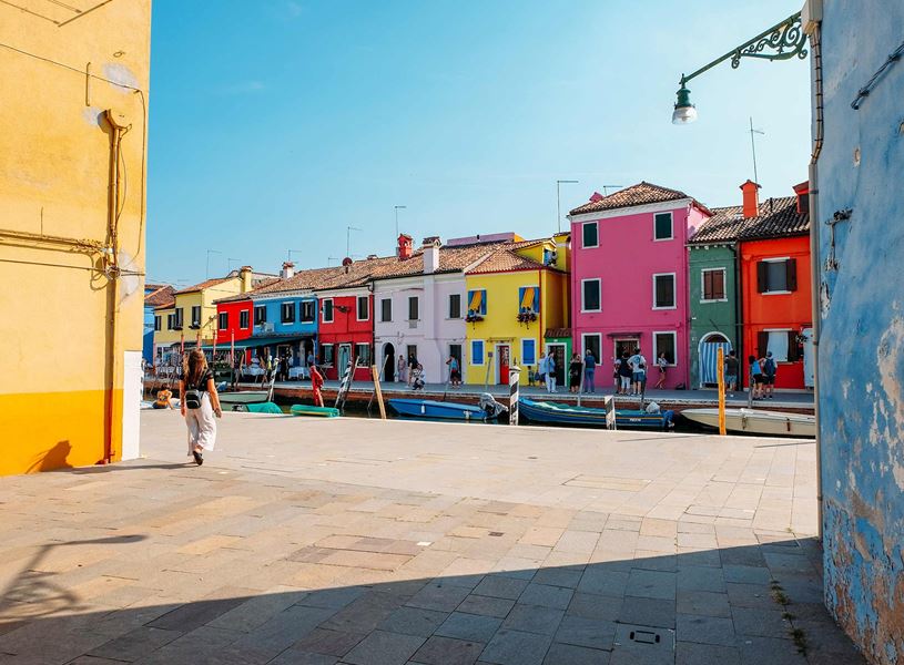Colourful buildings along canal in Burano with moored boats and pedestrians