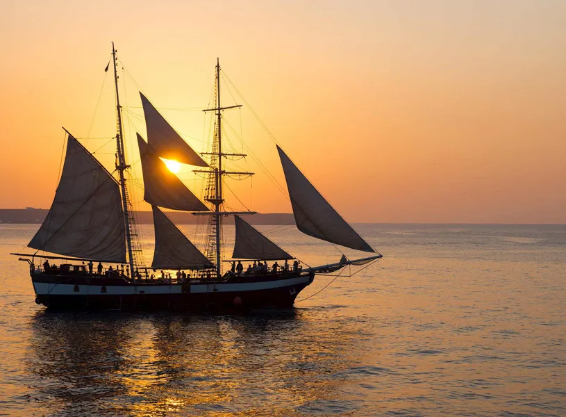 Silhouette of a sailing ship at sunset on calm sea waters