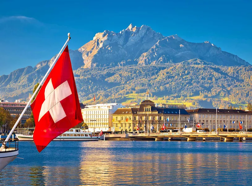Swiss flag on boat with Lucerne waterfront and Mount Pilatus backdrop in Switzerland