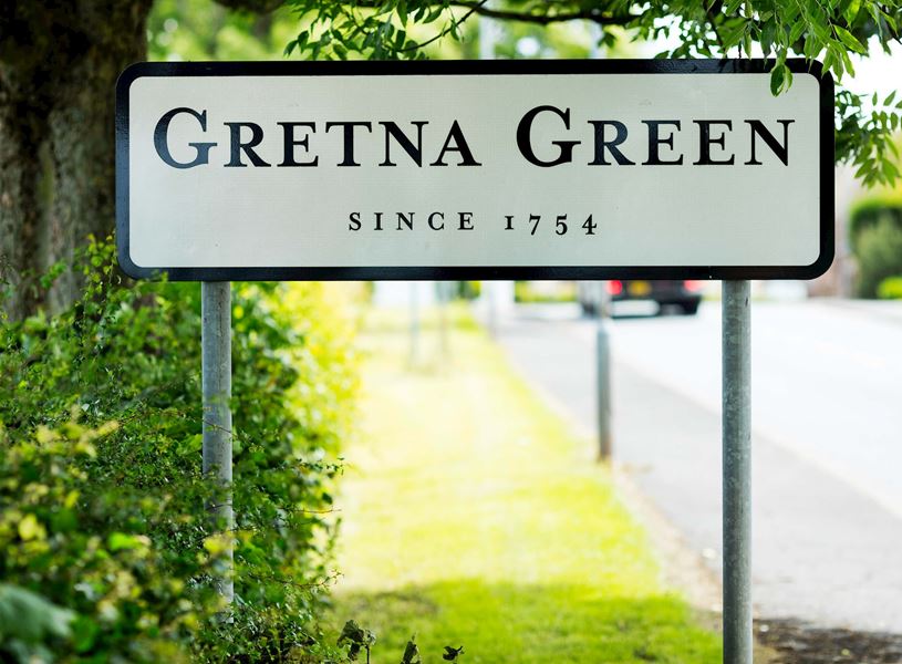 Gretna Green village sign on roadside surrounded by greenery